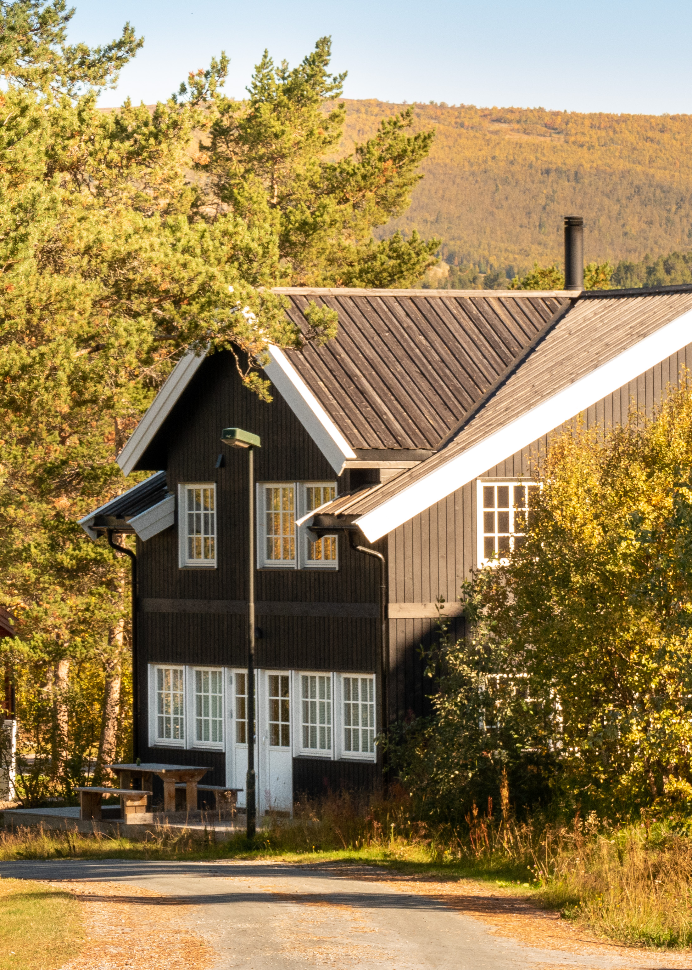 Eksteriør av stor hytte med grønn plen og grønne trær rundt. Foto