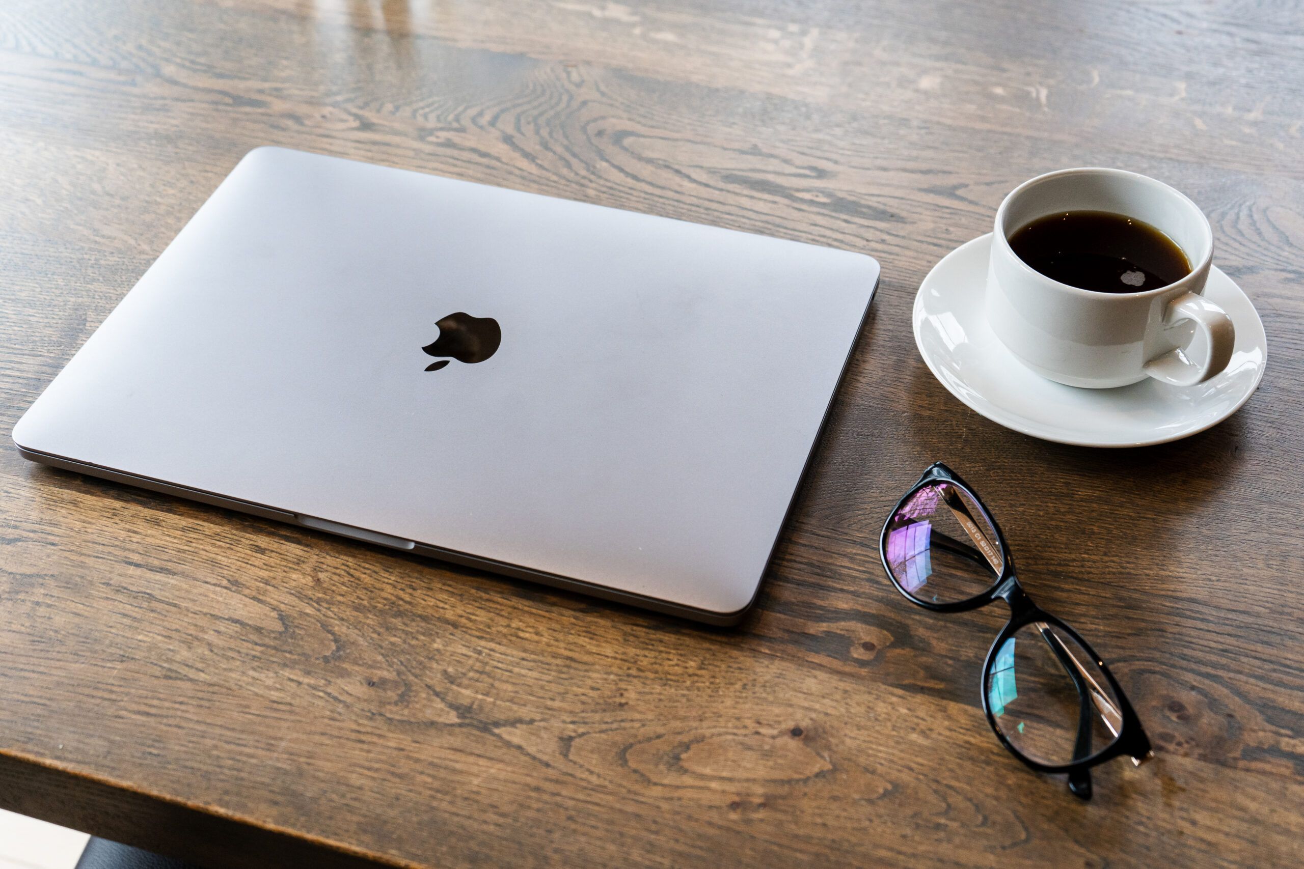 Laptop, kaffekopp og briller ligger på et bord. Foto